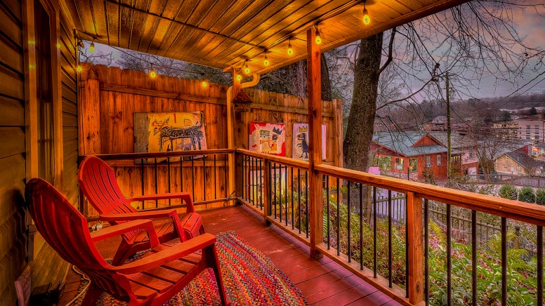 Porch with red Adirondack chairs at dusk with lit edison bulbs overhead overlooking downtown Blue Ridge.